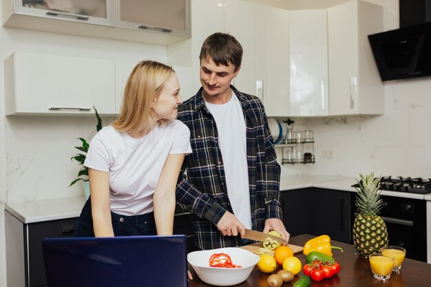 Feliz pareja preparando una cena saludable juntos en la cocina de su casa.