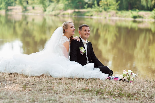 Feliz pareja de recién casados ​​jóvenes sentados en la hierba riendo juntos