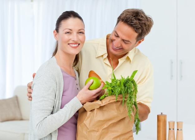 Feliz pareja regresa del mercado con frutas, verduras y pan