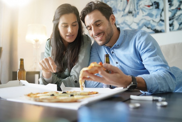 Feliz pareja relajada compartiendo una pizza en casa