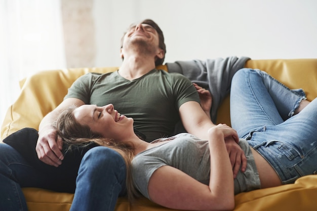 Feliz pareja relajándose en el sofá amarillo del salón de su nueva casa.