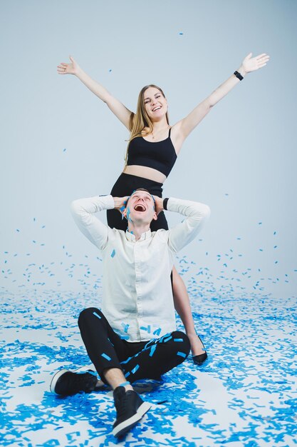 Feliz pareja riéndose de la fiesta de género mientras está sentada en confeti azul