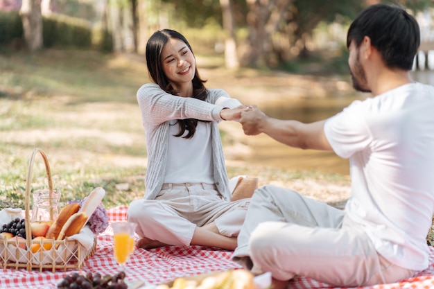 Feliz pareja romántica en el Día de San Valentín pareja asiática se dan la mano por un momento cercano juntos feliz pareja relajándose junto con picnic Basket