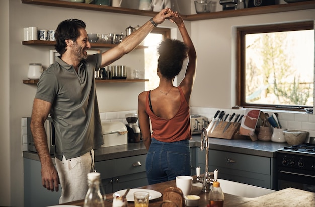 Feliz pareja romántica e interracial bailando y divirtiéndose mientras se une en la cocina en casa Una pareja amorosa despreocupada y enérgica que se siente alegre mientras comparte un baile y disfruta del tiempo juntos