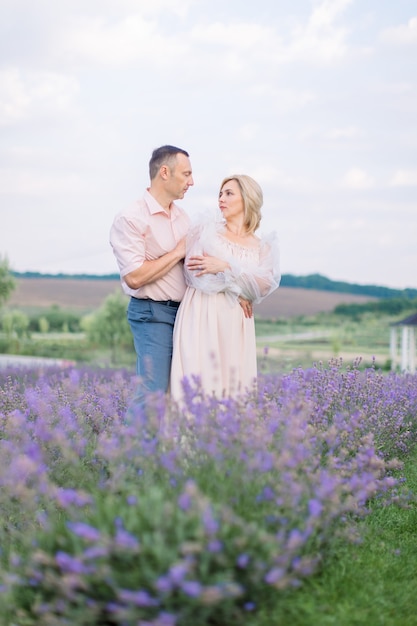 Feliz pareja romántica, posando juntos mirando el uno al otro, en el hermoso campo de lavanda