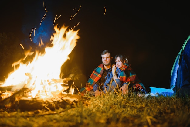 Feliz pareja romántica viajeros descansando en la hoguera cerca de la carpa turística brillante bajo el increíble cielo nocturno