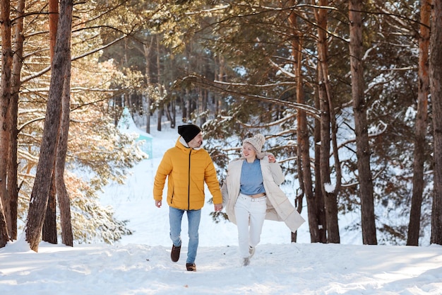 Feliz pareja en ropa de abrigo corriendo y divirtiéndose al aire libre en el bosque en invierno