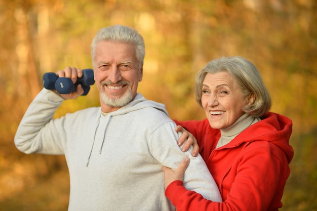 Feliz pareja senior de ajuste haciendo ejercicio con pesas en el parque de otoño