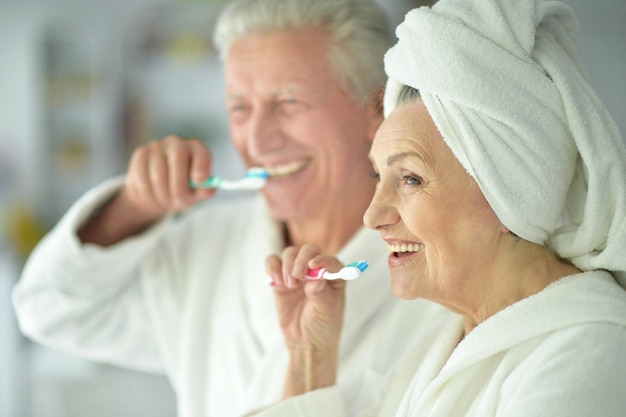 Feliz pareja senior en albornoces blancos cepillarse los dientes