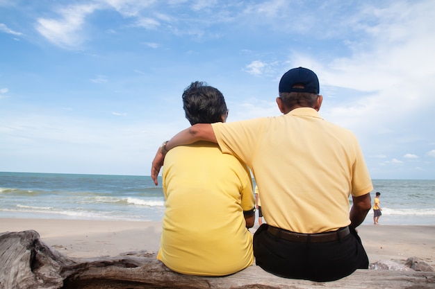 Feliz pareja senior asiática sentada y mirando a la playa, vista trasera