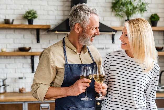 Feliz pareja senior bebiendo vino en la cocina mientras cocina