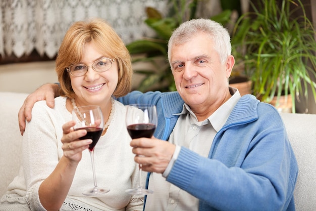 Feliz pareja senior brindando por su aniversario con vino tinto en el ambiente de casa