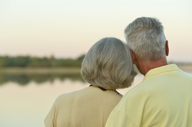 Feliz pareja senior cerca del lago durante la puesta de sol en verano