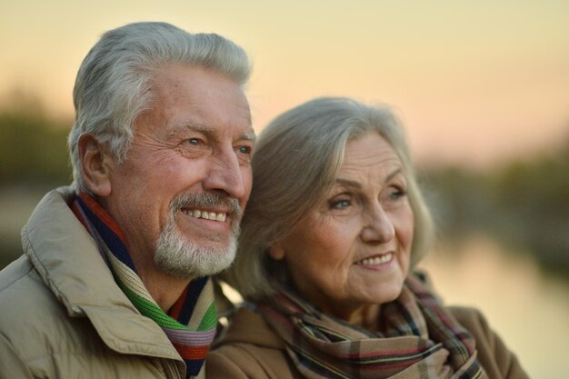 Feliz pareja senior cerca del río en otoño, fondo borroso