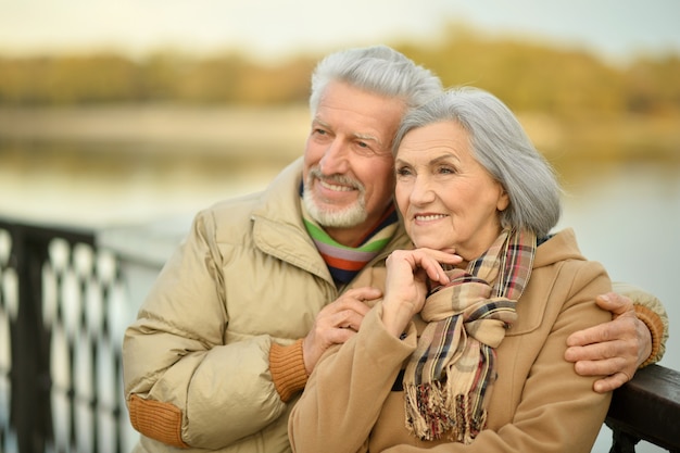 Feliz pareja senior cerca del río en otoño, fondo borroso