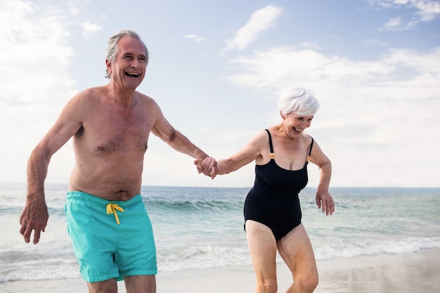 Feliz pareja senior cogidos de la mano y corriendo en la playa