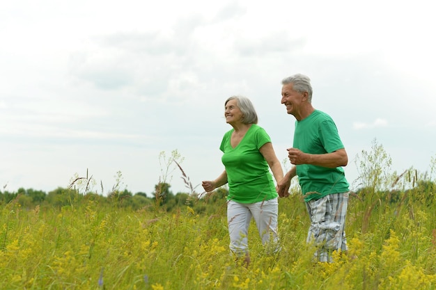 Feliz pareja senior corriendo en prado verde