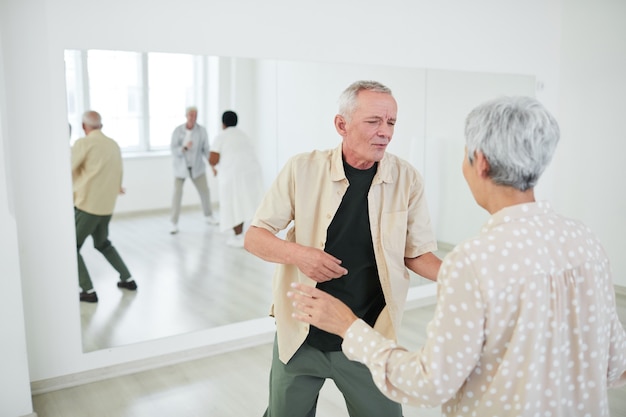 Feliz pareja senior divirtiéndose y bailando durante la lección en el estudio de baile con otras personas