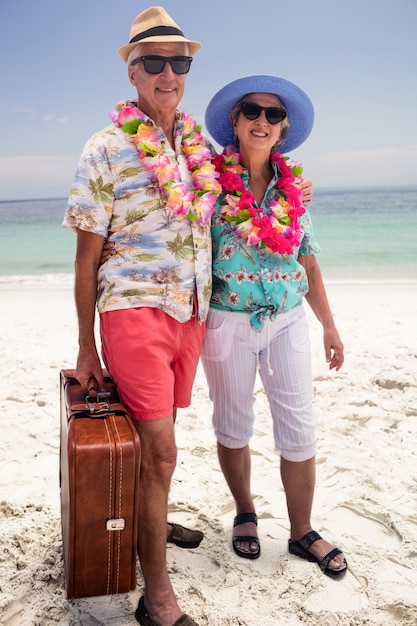 Feliz pareja senior con maleta en la playa