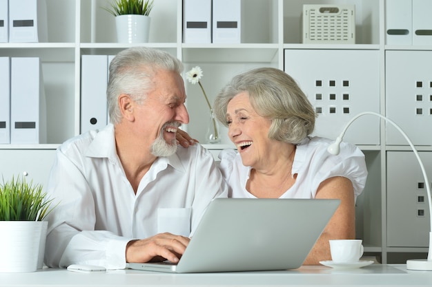 Feliz pareja senior con portátil en la oficina