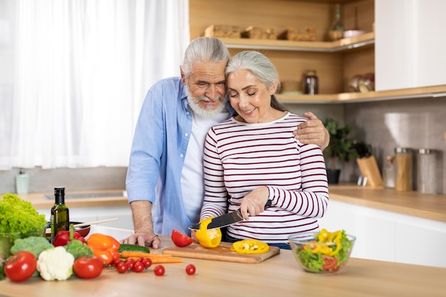 Feliz pareja senior preparando ensalada saludable juntos en el interior de la cocina
