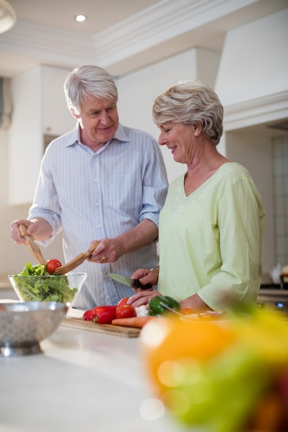 Feliz pareja senior preparando ensalada de verduras