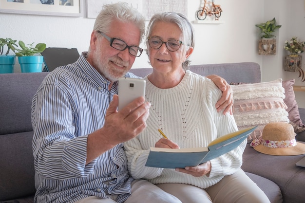 Feliz pareja senior sentado en un sofá en casa mediante teléfono móvil