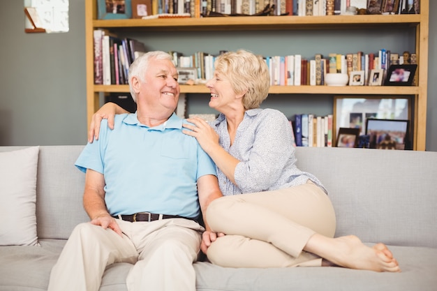 Feliz pareja senior sentado en el sofá contra la estantería