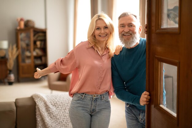 Foto feliz pareja senior sosteniendo la puerta abierta mirando a la cámara interior