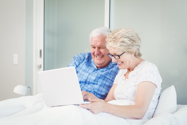 Feliz pareja senior usando laptop en la cama