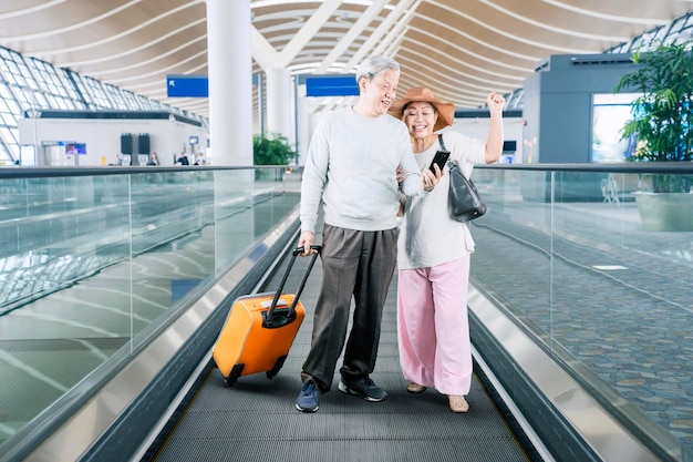 Feliz pareja senior usando un teléfono inteligente en el aeropuerto