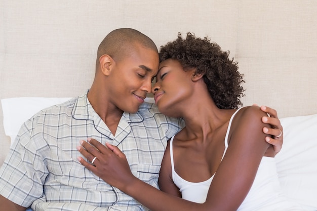 Feliz pareja sentada en la cama abrazados