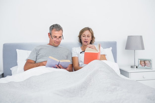 Feliz pareja sentada en la cama leyendo libros