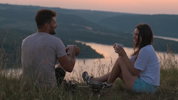 La feliz pareja sentada en la cima de la montaña y bebiendo té