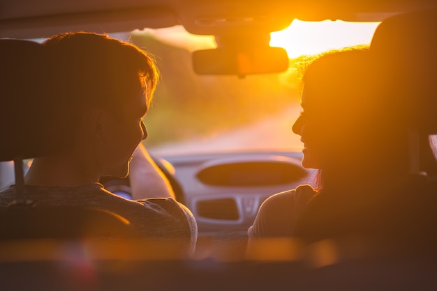 La feliz pareja sentada en un coche en el fondo de la puesta de sol