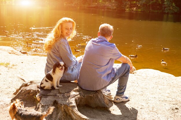 Feliz pareja sentada en el lago al sol con sus perros. Concepto de vacaciones familiares en la naturaleza.