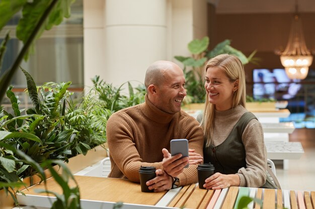 Feliz pareja sentada a la mesa en el restaurante tomando café y usando el teléfono móvil que recuerdan sus momentos felices