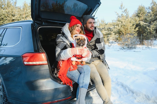 Feliz pareja sentada en la parte trasera del coche abierto, habiendo parada. Concepto de viaje romántico. Bosque de invierno.