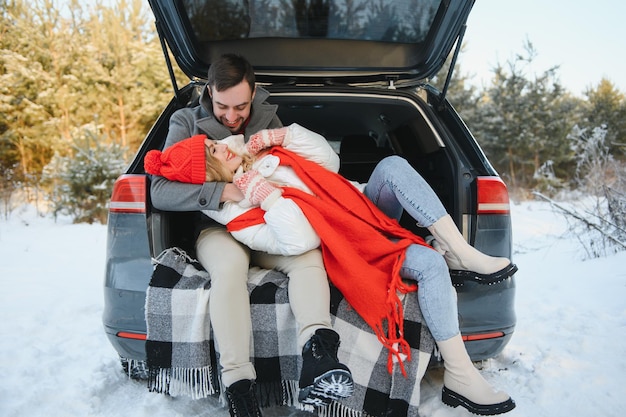 Feliz pareja sentada en la parte trasera del coche abierto, habiendo parada. Concepto de viaje romántico. Bosque de invierno.