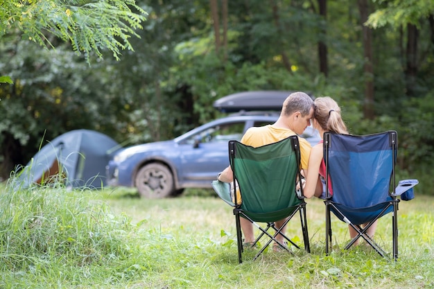 Feliz pareja sentada en sillas en el camping abrazándose juntos. Concepto de viajes, camping y vacaciones.