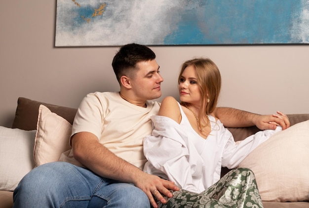 Feliz pareja sentada en el sofá en casa abrazándose y mirándose con ternura y amor hom