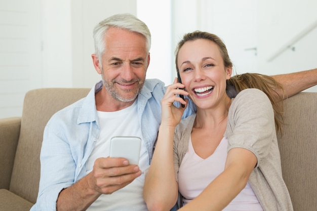Feliz pareja sentada en el sofá hablando y mensajes de texto en sus teléfonos