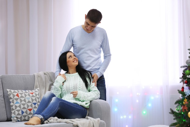 Feliz pareja sentada en un sofá en la sala de Navidad decorada