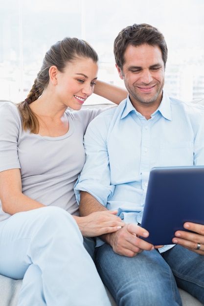 Feliz pareja sentada en el sofá con tablet pc