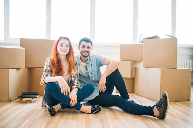 Feliz pareja sentada en el suelo entre cajas de cartón, mudarse a casa nueva, inauguración de la casa