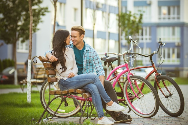 La feliz pareja se sienta en el banco cerca de las bicicletas