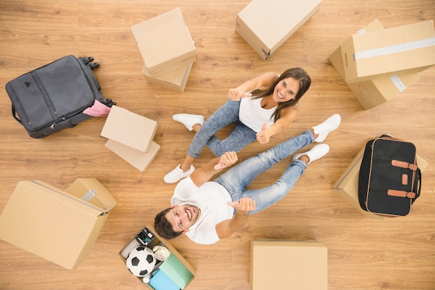 La feliz pareja se sienta cerca de cajas de cartón y gesticula. vista desde arriba