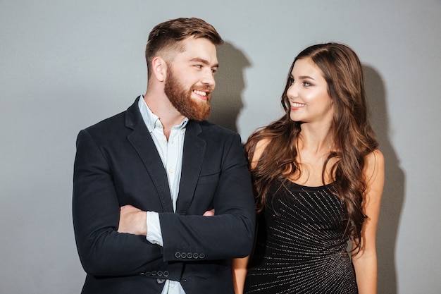 Feliz pareja sonriente en ropa formal mirando el uno al otro sobre pared gris