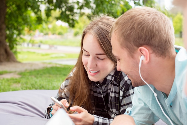 Feliz pareja sonriente salir al aire libre, tendido en un cojín y mirando el teléfono celular.