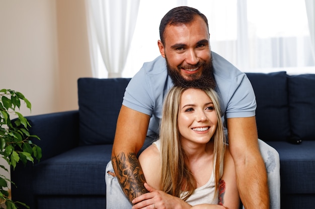Feliz pareja sonriente sentada en un sofá azul en la sala de estar